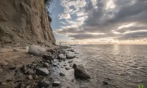 Klif w Gdyni, kamienista plaża i morze. W oddali widać statki. To jedna z pięknych gdynia atrakcji.