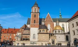Majestatyczna katedra wawelska z cegły i kamienia, z dominującą wieżą i złotą kopułą, na tle błękitnego nieba.