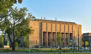 Muzeum Narodowe w Krakowie przy Alei 3 Maja. Monumentalna budowla z kamienia, otoczona zielenią i stojakami z hulajnogami.