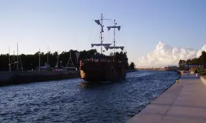 Żaglowiec w kształcie pirackiego statku wpływa do portu w Łebie. Widoczny betonowy brzeg i drzewa.