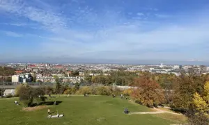 Jesienny dzień w Krakowie. Ludzie odpoczywają na zielonej trawie, a w tle rozciąga się panorama miasta.