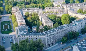 Osiedle w stylu socrealistycznym, przypominające architekturę Nowej Huty, z zielenią i ulicą z tramwajem.