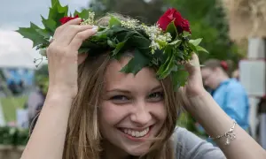 Uśmiechnięta dziewczyna w wianku z czerwonych róż i zielonych liści, jak na krakowskim festynie.