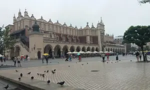 Deszczowy dzień na Rynku Głównym w Krakowie. Ludzie z parasolami spacerują, szukając schronienia w Sukiennicach lub kawiarniach. To świetny pomysł, co robić w Krakowie, gdy pada.