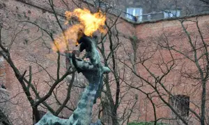 Pomnik smoka wawelskiego zieje ogniem na tle ceglanej ściany.