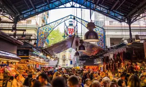 Tętniący życiem Mercat de la Boqueria w Barcelonie, pełen ludzi, kolorowych stoisk z jedzeniem i charakterystycznego, ozdobnego łuku.