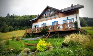Dom z drewnianym tarasem i hamakiem w ogrodzie, otoczony zielenią. Idealne miejsce, by odpocząć i zastanowić się, gdzie w Bieszczady.