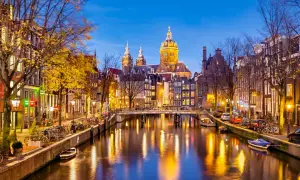Wieczorne atrakcje Amsterdamu: malowniczy kanał z odbijającymi się światłami, most, rowery i zabytkowa architektura.