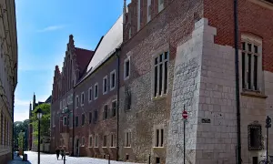 Kamienne i ceglane mury Collegium Maius w Krakowie, z charakterystycznymi oknami i detalami architektonicznymi, na tle błękitnego nieba.