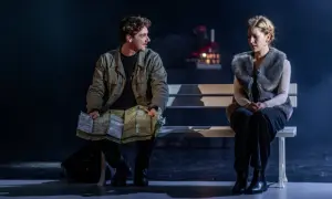 Para na ławce, mężczyzna z mapą, kobieta w futrzanej kamizelce. Scena z dramatu "Jelegnia Góra" pełna napięcia.