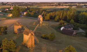 Wielkopolska atrakcje: drewniane wiatraki na tle zachodzącego słońca, malowniczy krajobraz wsi i pól.