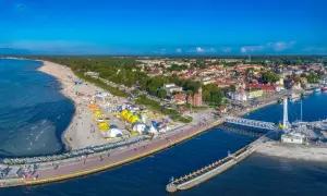 Ustecka plaża tętni życiem, pełna kolorowych namiotów i ludzi. W tle widać urokliwe miasteczko i port. To idealne ustka atrakcje dla każdego.