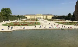Piękny park w Wiedniu z pałacem w tle i ludźmi spacerującymi po kwiecistych rabatach.