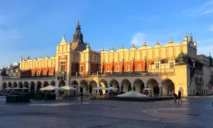 Sukiennice Kraków w blasku słońca, z arkadami i wieżą zegarową. Rynek tętni życiem.