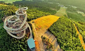 Drewniany sky bridge w Czechach wije się wśród zielonych lasów, oferując widok na złote pola i góry.