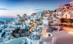 Santorini nocą, z białymi domkami, wiatrakami i grecką flagą, w blasku zachodzącego słońca.
