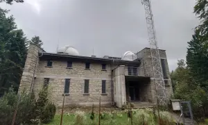Obserwatorium na Lubomirze, kamienny budynek z kopułami i wieżą telekomunikacyjną, otoczony zielenią.