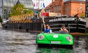 Para wodna w Bydgoszczy: młoda para w zielonym samochodziku-łódce, na wodzie, z napisem "BYDGOSZCZ" na barce w tle. To świetne bydgoszcz atrakcje!