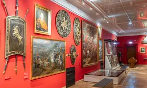Wnętrze muzeum w Krakowie z obrazami historycznymi, portretem i zbrojami na czerwonych ścianach.
