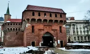 Imponujący barbakan kraków z cegły, z charakterystycznymi łukami i blankami, otoczony zimowym krajobrazem.