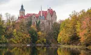 Zamek Książ w jesiennej odsłonie, idealne miejsce na jednodniowy wypad w Polsce. Otoczony kolorowymi drzewami, odbija się w spokojnej tafli wody.