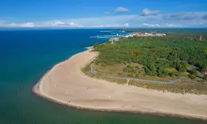 Piękne, piaszczyste plaże i zielone lasy otaczają urokliwe hel miasto. W oddali widać port i zabudowania.