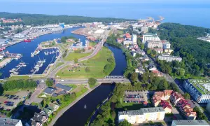 Widok z lotu ptaka na port i rzekę w Kołobrzegu. Widoczne liczne jachty, mosty, budynki mieszkalne i tereny zielone. Kołobrzeg atrakcje turystyczne w pełnej krasie.