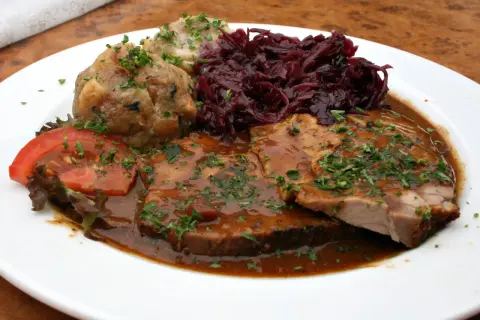 Pyszne jedzenie w Niemczech: pieczeń wieprzowa w sosie, kluski ziemniaczane, czerwona kapusta i pomidor.