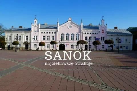 Różowy budynek ratusza na rynku w Sanoku, z napisem "Sanok najciekawsze atrakcje".