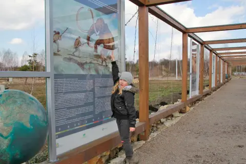 Dziewczynka wskazuje na tablicę informacyjną o prehistorii, jedną z atrakcji Jaworzna. Obok globus.