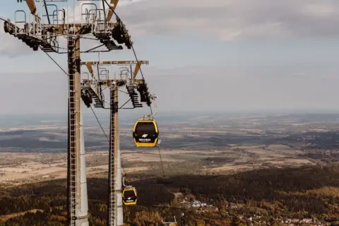 Kolejka linowa, niczym żółty roller coaster, wznosi się nad jesiennym krajobrazem.