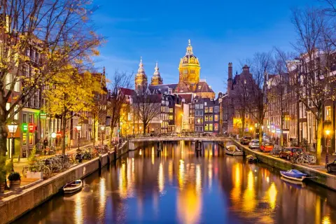Wieczorne atrakcje Amsterdamu: malowniczy kanał z odbijającymi się światłami, most, rowery i zabytkowa architektura.