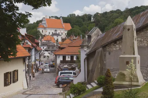 Urokliwa ulica w Kazimierzu Dolnym z kościołem na wzgórzu. Kamienne bruki, kamienice z czerwonymi dachami i zielone drzewa tworzą malowniczy krajobraz.