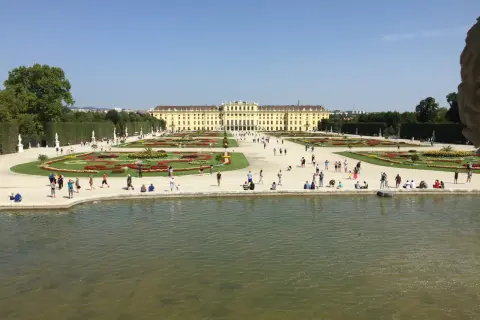 Piękny park w Wiedniu z pałacem w tle i ludźmi spacerującymi po kwiecistych rabatach.