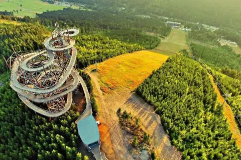 Drewniany sky bridge w Czechach wije się wśród zielonych lasów, oferując widok na złote pola i góry.