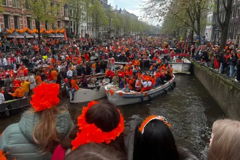 Tłumy ludzi w pomarańczowych strojach świętują dzień króla w Amsterdamie, płynąc łodziami po kanałach.