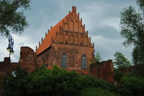 Gotycka ceglana bazylika z czerwonym dachem, ruiny murów obronnych i zieleń. To jedno z miejsc, co zobaczyć w Elblągu.