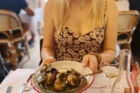 Paryż jedzenie: kobieta w letniej sukience serwuje ślimaki w restauracji, obok kieliszek białego wina.