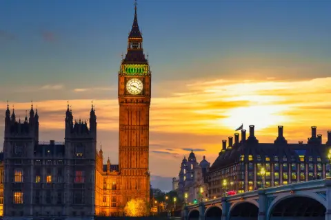 Wieża zegarowa Big Ben w Londynie o zachodzie słońca, z Parlamentem i mostem w tle.