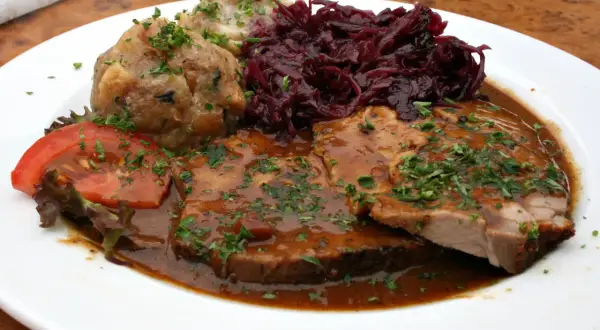 Pyszne jedzenie w Niemczech: pieczeń wieprzowa w sosie, kluski ziemniaczane, czerwona kapusta i pomidor.