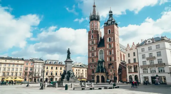 Rynek Główny w Krakowie z Kościołem Mariackim i pomnikiem Mickiewicza. Stare miasto Kraków tętni życiem pod błękitnym niebem.