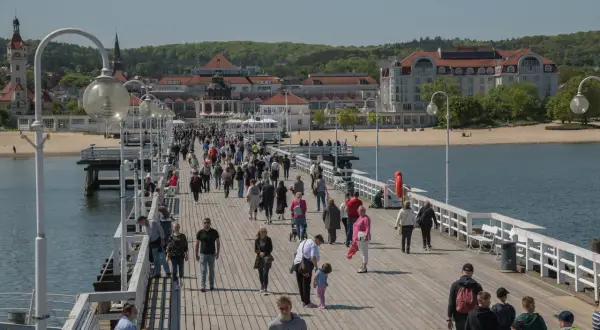 Spacer po molo w Sopocie, pełnym ludzi, to jedna z **nietypowych atrakcji Gdańska** i okolic. W tle widać plażę i zabytkowe budynki.