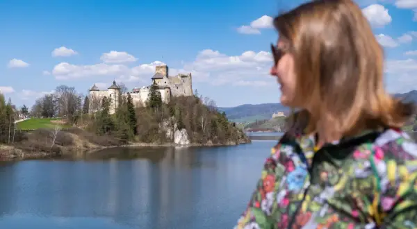 Widok na zamek nad jeziorem, z kobietą w kolorowej kurtce na pierwszym planie. To wspaniałe niedzica atrakcje turystyczne.