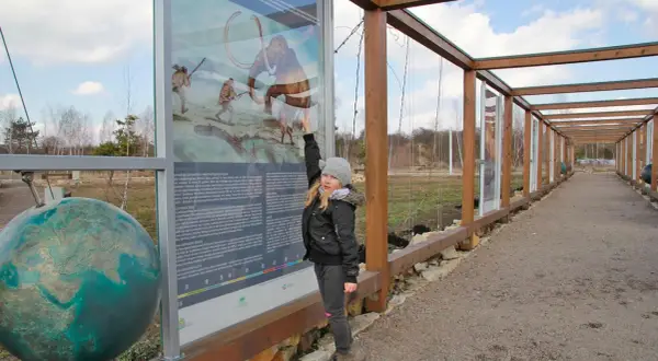 Dziewczynka wskazuje na tablicę informacyjną o prehistorii, jedną z atrakcji Jaworzna. Obok globus.