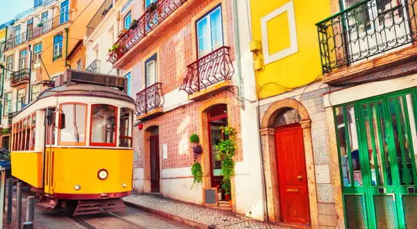 Żółty tramwaj przemierza ulicę w Lizbonie w marcu, mijając kolorowe kamienice z azulejos i ozdobnymi balkonami.