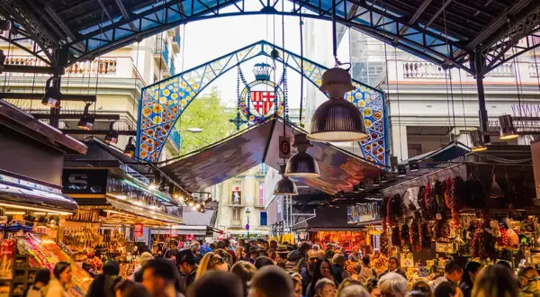 Tętniący życiem Mercat de la Boqueria w Barcelonie, pełen ludzi, kolorowych stoisk z jedzeniem i charakterystycznego, ozdobnego łuku.