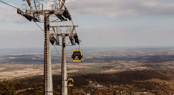 Kolejka linowa, niczym żółty roller coaster, wznosi się nad jesiennym krajobrazem.