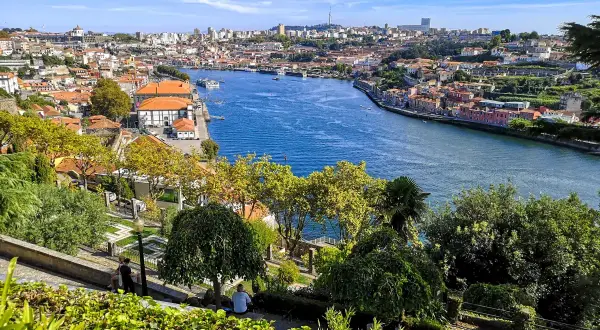 Widok na rzekę Duero i zabytkowe centrum Porto. Widać łodzie, kolorowe kamienice i zielone wzgórza. To idealne miejsce na podziwianie porto atrakcje.