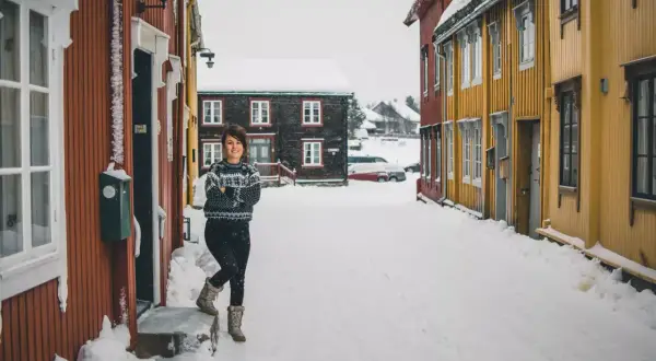 Uśmiechnięta kobieta w swetrze stoi na zaśnieżonej ulicy w Oslo zimą.