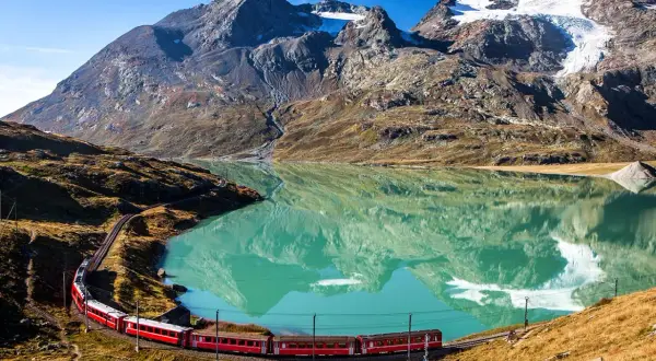 Czerwony pociąg przemierza malownicze szwajcaria widoki, odbijając się w turkusowym jeziorze u stóp gór.